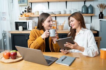 Two women read books, use laptops to work, kitchen