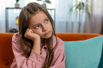 Portrait of calm brunette little girl sitting alone on couch in living room at home. Preteen...