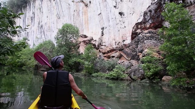 Kayaker wields paddle guiding kayak along river flow waving hand to holidaymakers on land. Active summer weekend amidst canyon and forest