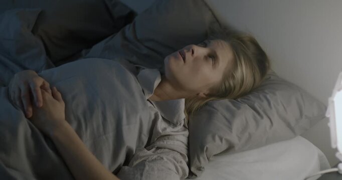 Angry young woman can't sleep because of loud noise suffering in bed covering ears with pillow at sleepless night. Sleep disorder and people concept.