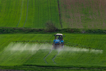 Fototapeta premium Aerial view of tractor spraying crop in green farm fields with pesticide