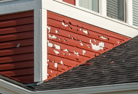 A close-up of a building's exterior shows red siding with extensive hail damage, exposing the underlying white surface.
