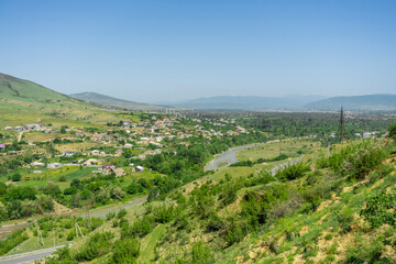 View from above on the river Ksani, on the village along the river, plains covered with grass and bushes. Mountains and blue sky in the background