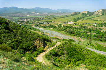 View from above on the river Ksani, on the village along the river, plains covered with grass and bushes. Mountains and blue sky in the background