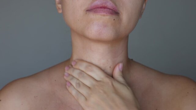 Young woman applying anti-wrinkle serum to the neck and cleavage area to moisturize the skin smearing it with her hand on a grey background. Wrinkles, lines, age-related changes, anti-aging procedures