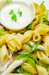 A box of takeaway with pasta, a white sauce and green vegetables
