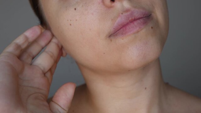 Young caucasian woman pressing on the ear trying to get rid of congestion on a grey background. The problem of sulfur plugs. The girl suffering from ear pain