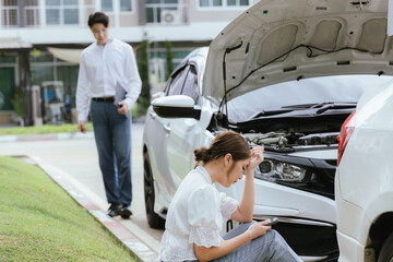 A young Caucasian man and an Asian woman inspect a damaged car after an auto accident. The insurance agent examines the vehicle, writing a report while gathering evidence for the claim investigation a