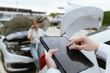 A young Caucasian man and an Asian woman inspect a damaged car after an auto accident. The insurance agent examines the vehicle, writing a report while gathering evidence for the claim investigation a