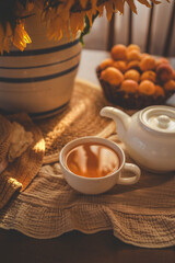 Pouring tea from a white teapot into a cup, with a bouquet of sunflowers in the background. The warm, soft lighting creates a cozy and calming atmosphere, perfect for a peaceful tea time