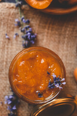 Homemade apricot jam with lavender flowers, surrounded by fresh apricots and lavender sprigs on a rustic burlap cloth