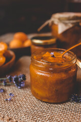 Homemade apricot jam with lavender flowers, surrounded by fresh apricots and lavender sprigs on a rustic burlap cloth