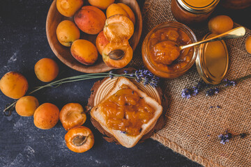 Homemade apricot jam with lavender flowers, surrounded by fresh apricots and lavender sprigs on a rustic burlap cloth
