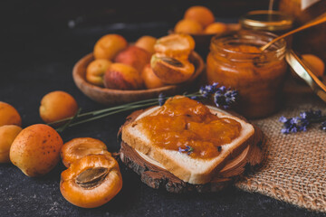 Homemade apricot jam with lavender flowers, surrounded by fresh apricots and lavender sprigs on a rustic burlap cloth