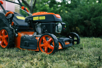 Bright orange lawn mower on a freshly cut lawn in a garden. The machine stands out against the greenery, showcasing its modern design and functionality for outdoor lawn maintenance