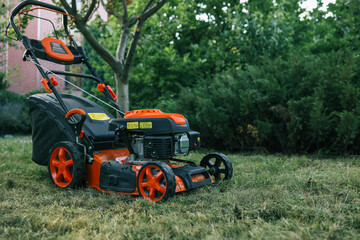 Bright orange lawn mower on a freshly cut lawn in a garden. The machine stands out against the greenery, showcasing its modern design and functionality for outdoor lawn maintenance