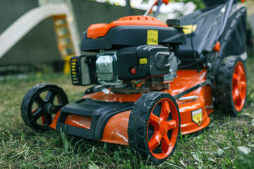 Bright orange lawn mower on a freshly cut lawn in a garden. The machine stands out against the greenery, showcasing its modern design and functionality for outdoor lawn maintenance