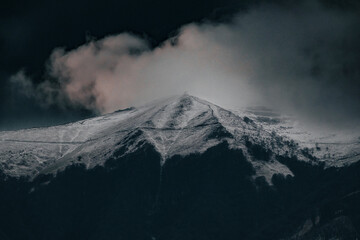 Majestic snow-covered mountain peak shrouded in dramatic clouds, creating a moody and atmospheric alpine landscape.