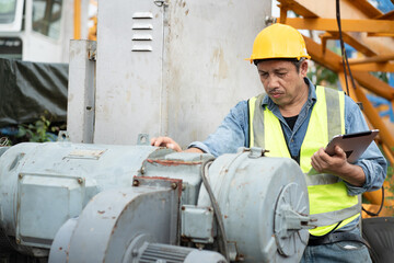 Asia engineer man worker checking machine and use tablet computer with spare crane background	