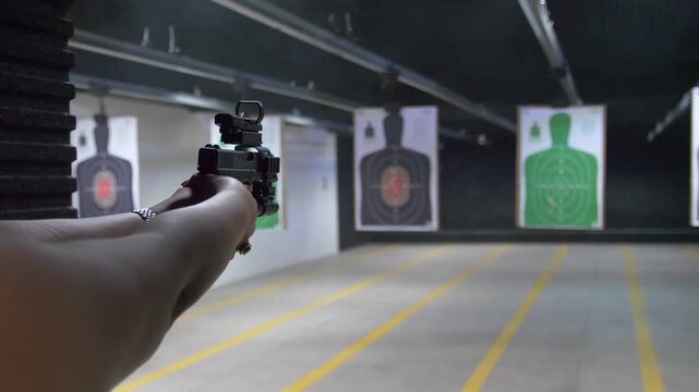 Shooting range practice. Woman shooting with tactical handgun at indoor targets.