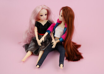 Two common plastic female dolls sitting near on pink background. Friendships and lesbian couple concept.