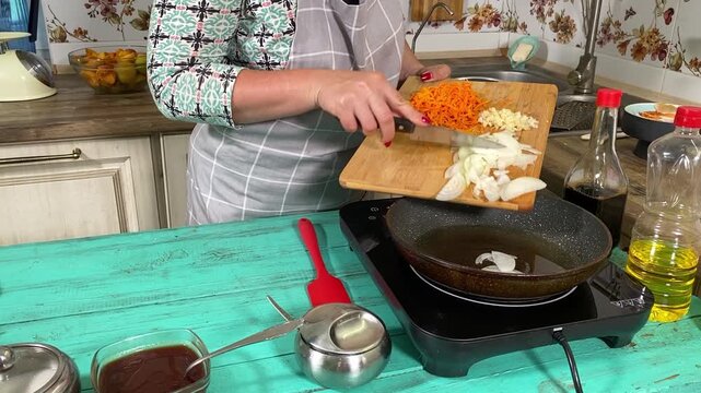 Culinary concept, preparation ingredients for homemade food. A young adult beautiful woman in an apron cooking a meal, makes mirepoix on a kitchen counter indoors. Home cooking and gastronomy passion