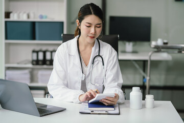 Doctor working on laptop computer and tablet and medical stethoscope on clipboard on desk, electronics medical record system EMRs concept.