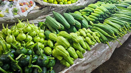Fresh green vegetables, including gourds and cucumbers at a local market stall