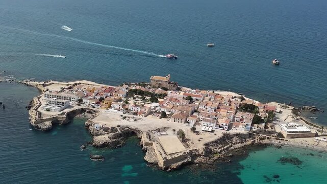 Aerial views of Spanish island Tabarca. Sunny day, turquoise waters, yachts in the cove. Calm sea, city and beach bustling with tourists. Costa Brava hotspot.