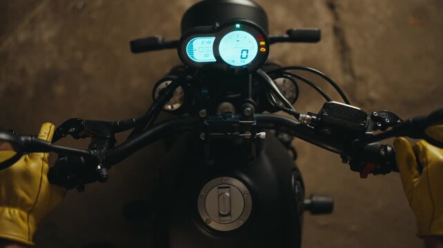 Close-up top view of a mechanic in yellow gloves starting a motorcycle and inspecting its glowing panel in the workshop