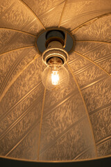 Turned on, incandescent lightbulb inside fabric, ceiling hanging cover. Close up shot, no people