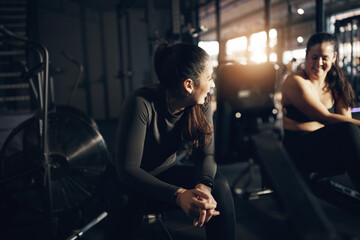 Fit young woman in sportswear talking with a female friend during a break from a workout on a rowing machine during a gym exercise class