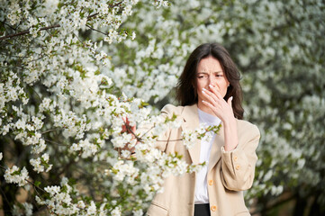 Woman allergic suffering from seasonal allergy at spring in blossoming garden at springtime. Young...