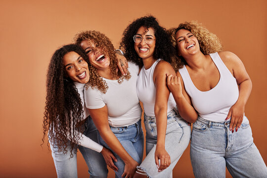 Diverse women in jeans and white tops laughing together on an orange background