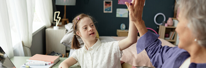 Header image of young girl with Down syndrome giving high five to grandmother while doing homework...