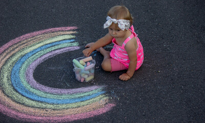 Naklejka premium a little girl draws a rainbow on the asphalt with chalk. Selective focus