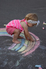 Fototapeta premium a little girl draws a rainbow on the asphalt with chalk. Selective focus