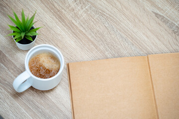 Cup of hot coffee with an open mock up magazine or blank book on a wooden table or desk from above.
