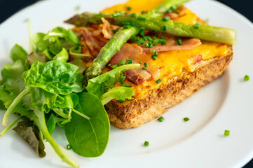 Fried toast with bacon and cheese, asparagus and fresh salad leaf on white plate, closeup.