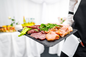 A waiter holding a tray with assorted sliced meats garnished with green leaves, set in a banquet environment. Ideal for catering, hospitality, and food service themes.