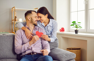 Married couple spending Valentine's Day at home. Happy man and woman having good time together, giving each other heart shaped paper Valentine cards, hugging, kissing and having fun. Love concept
