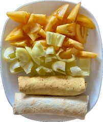 A dish featuring chopped chicken wrapped in lavash, paired with yellow tomatoes and sliced yellow bell peppers on a white plate, offering a colorful and healthy meal option.