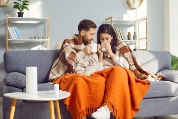 Young couple wrapped in blankets sitting on sofa at home. Happy lovers couple sitting together...