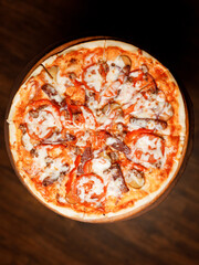 delicious pizza with juicy sausages, fresh vegetables, creamy cheese, and thin crust on a beautiful wooden table in a cozy nice restaurant