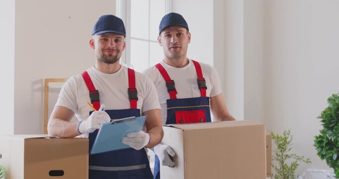 Moving service, happy professional movers with cardboard box, load, pack, unload item with care among stacked paper moving containers, unpacking stuff after relocation into new apartment, flat, office