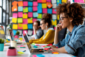 A creative team members are seen brainstorming around a table, filled with laptops, colorful sticky notes, and planning materials, fostering an energetic work atmosphere.