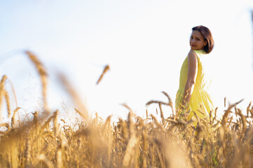 pretty young girl standing in wheat field, back looking over shoulder smiling, wearing yellow vog dress, place for writing, fields and nature of Ukraine