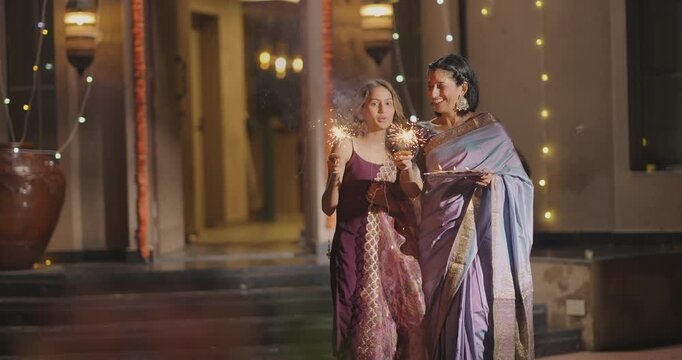 Indian Hindu Asian happy cute teen child girl young adult female old aged elder mom hold crackers make fun joy enjoy play Diwali festive season spend night time decor lights diya outdoor home house