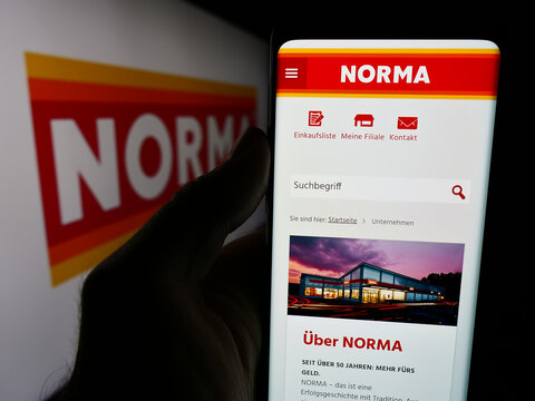 Stuttgart, Germany - 08-05-2024: Person holding mobile phone with website of company Norma Lebensmittelfilialbetrieb Stiftung Co. KG with logo. Focus on center of phone display.