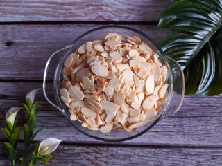 Bowl of sliced almonds placed on a wooden table, with green leaves peeking in the corner, underscoring the focus on food, ingredients, and healthy eating.
